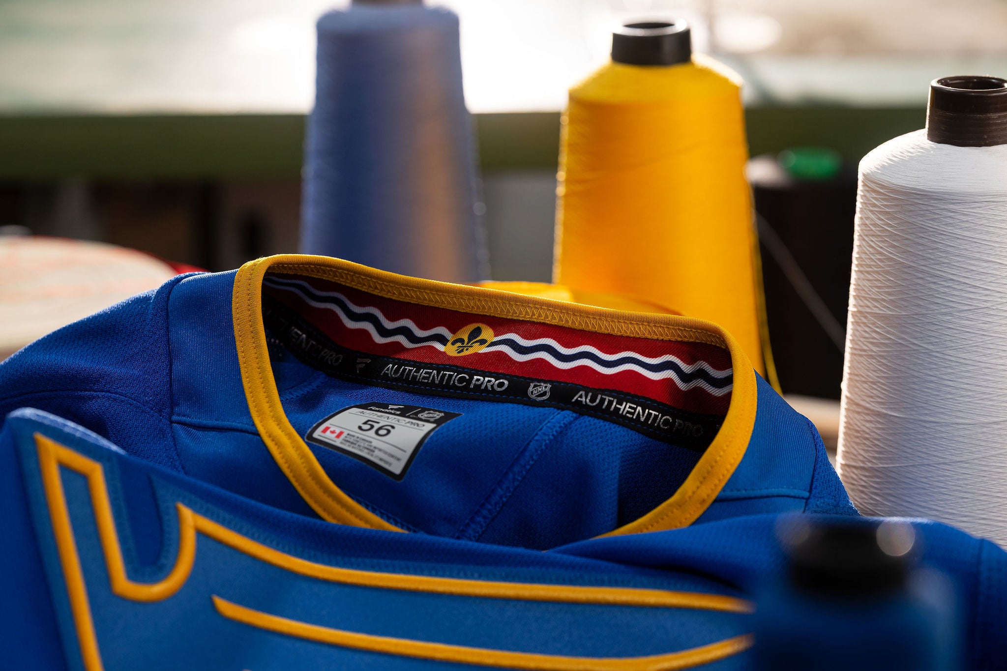 Blue sports jersey with yellow accents and visible brand labels, surrounded by spools of thread.