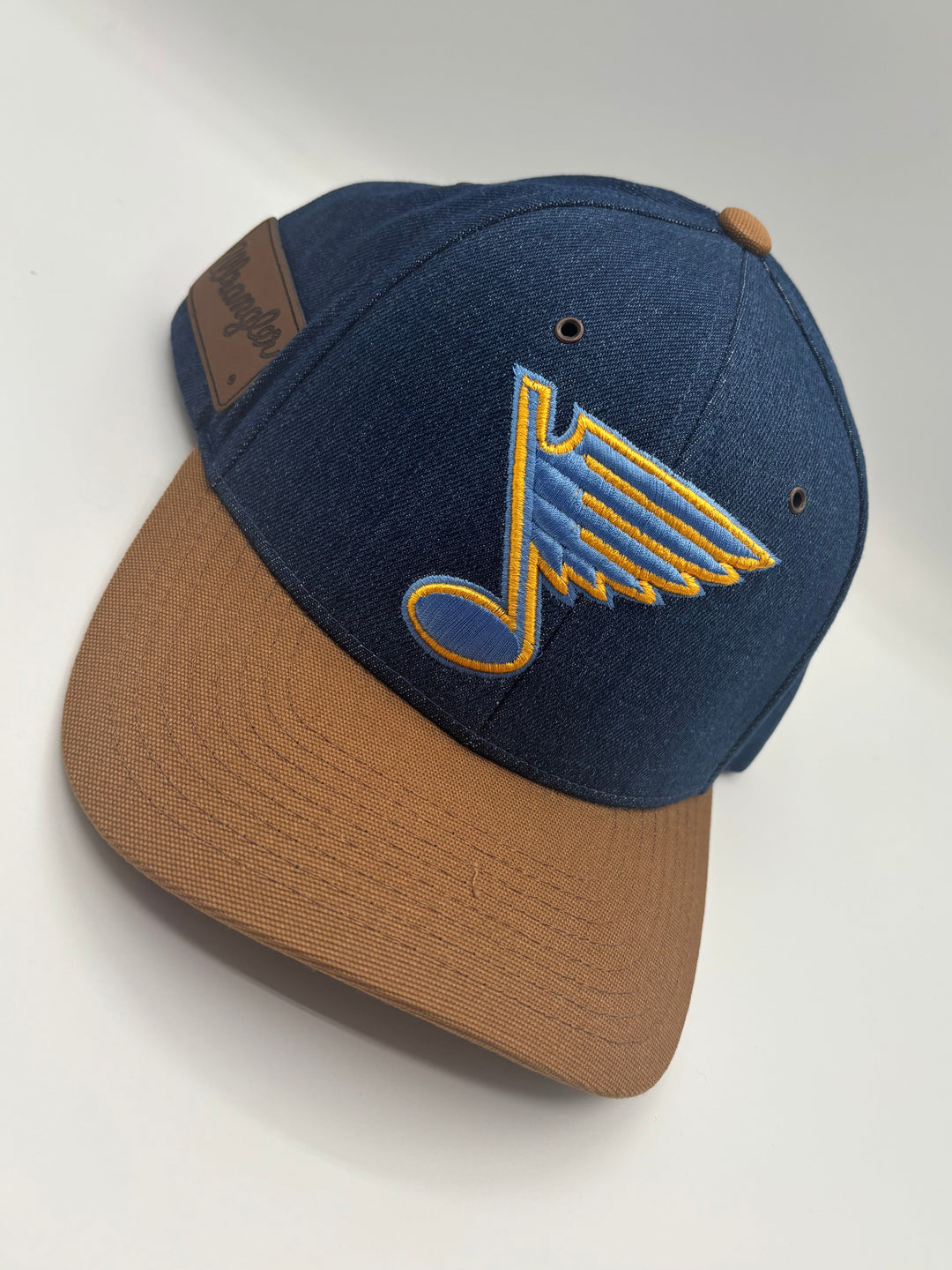 A St. Louis Blues baseball cap with a navy blue crown, a tan visor, and a blue and yellow embroidered logo on the front.